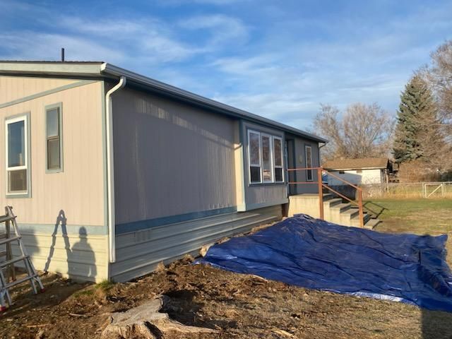 Mobile home exterior, partially repainted, blue siding and trim. Blue tarp covers the ground.