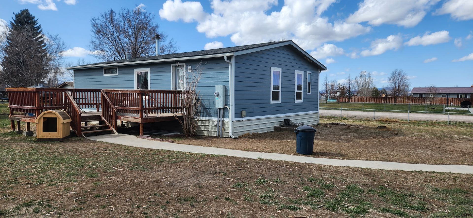 Blue house with a deck and dog house in a yard.