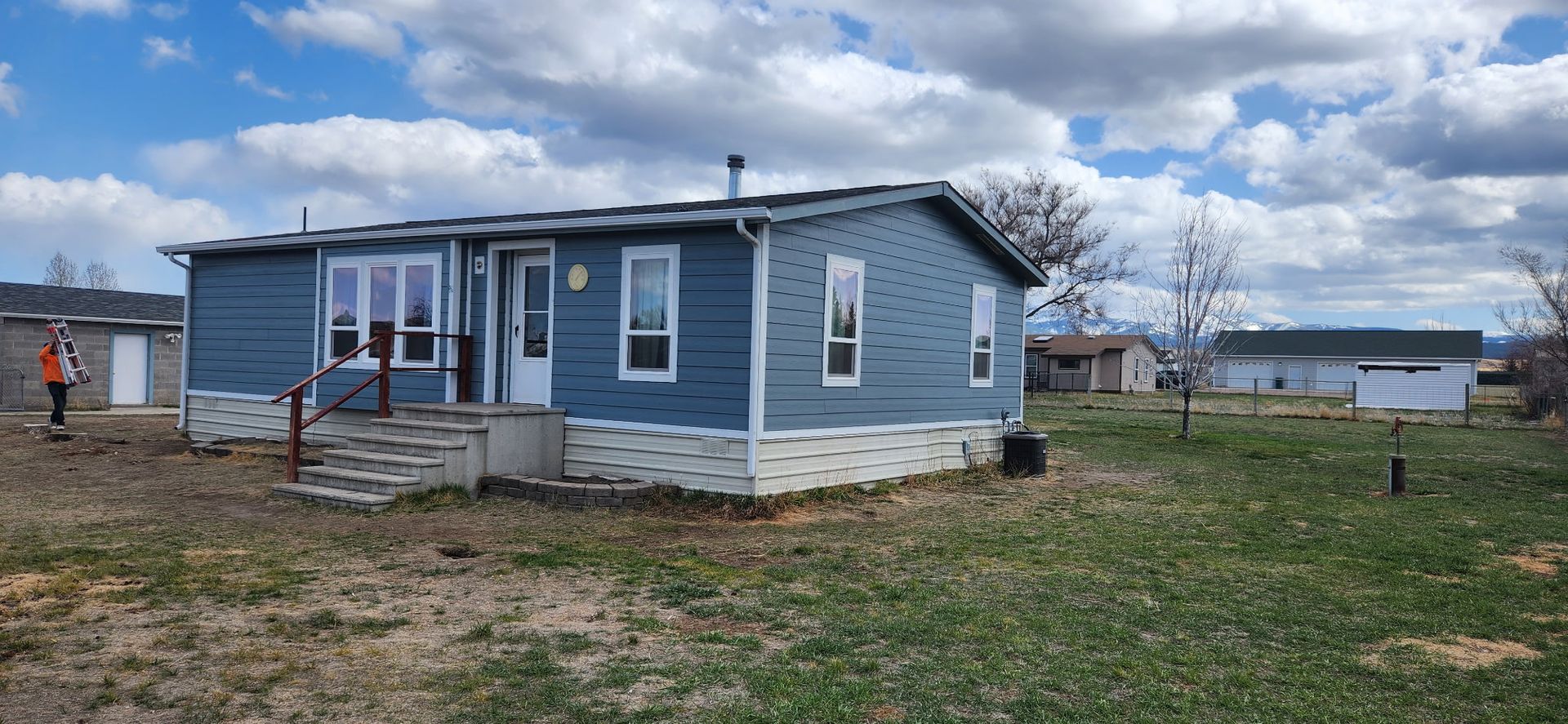 Blue-sided home with white trim and a small porch on a grassy lot under a cloudy sky.
