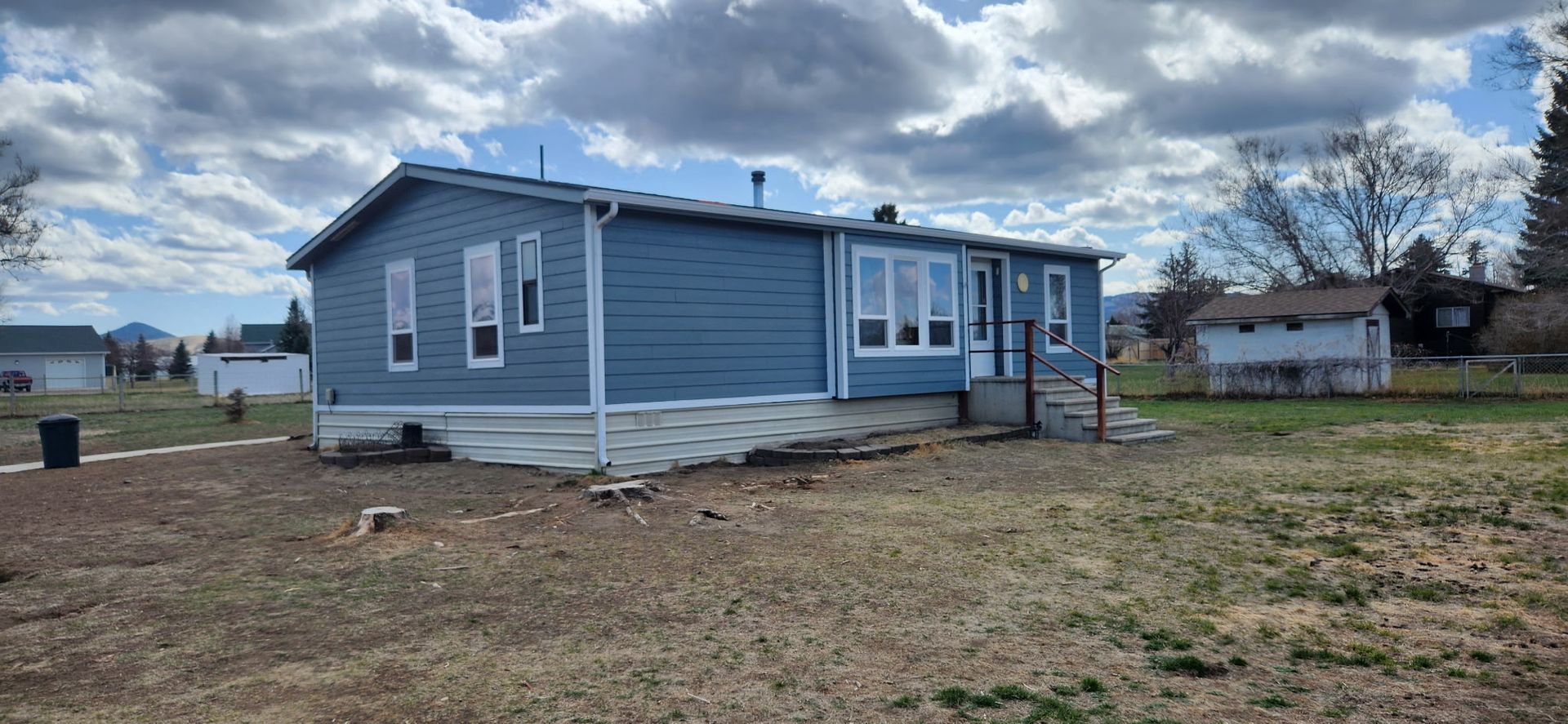 Blue house with white trim under a cloudy sky. Brown yard.