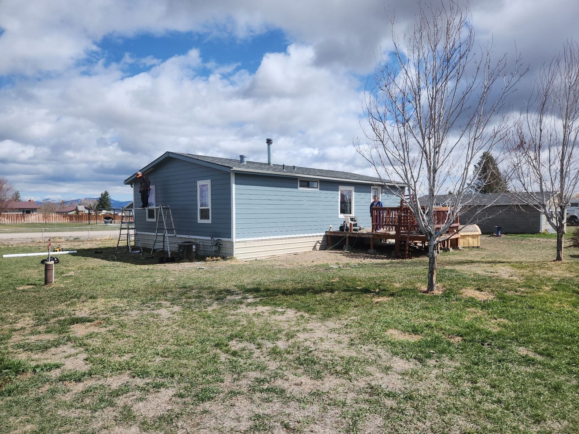 Blue house with a deck in a grassy yard under a cloudy sky.