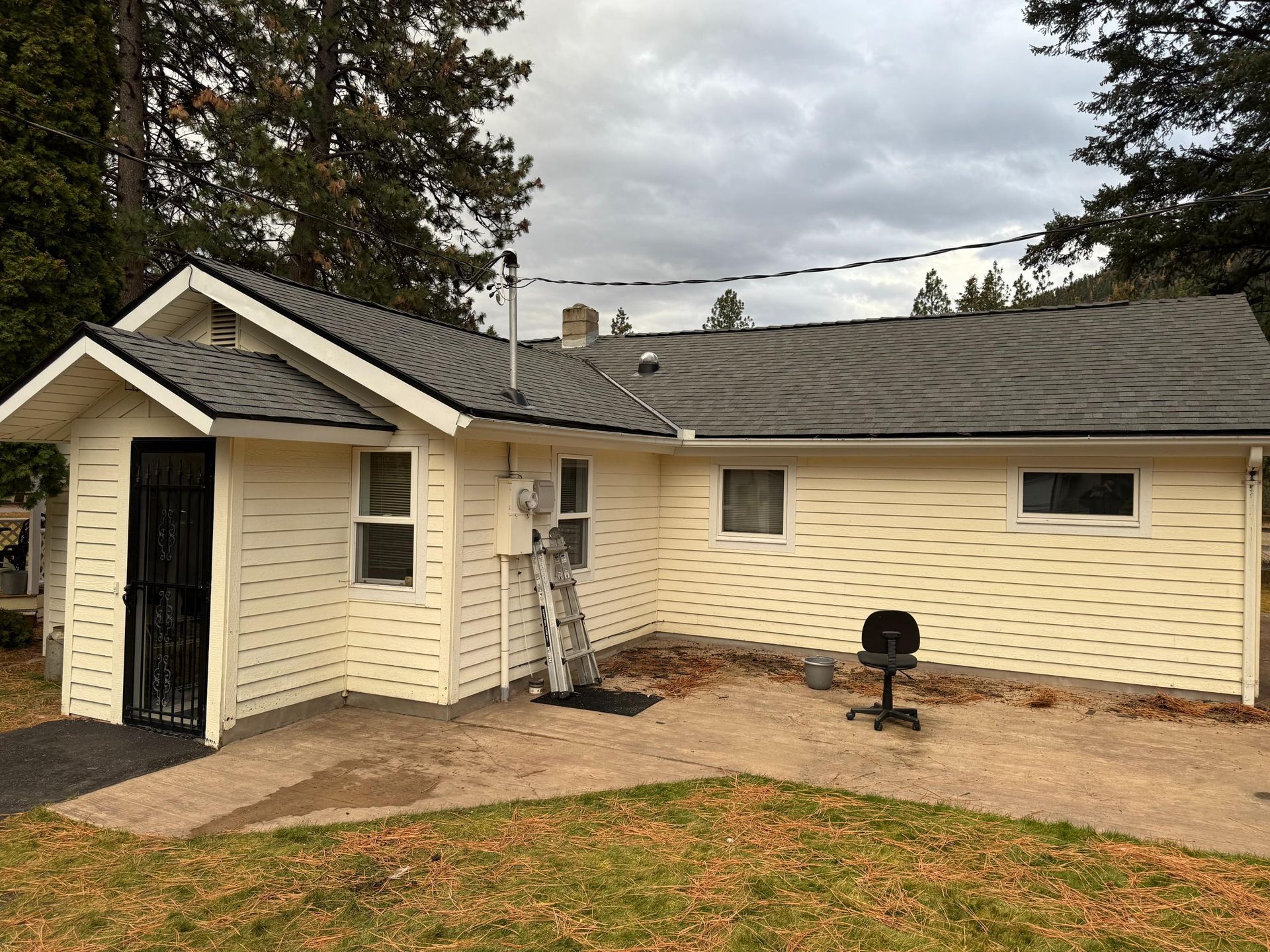 Beige house with gray roof; black door, windows, chair outside. Overcast day.