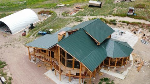 Aerial view of a house under construction with a green metal roof and wooden framing.