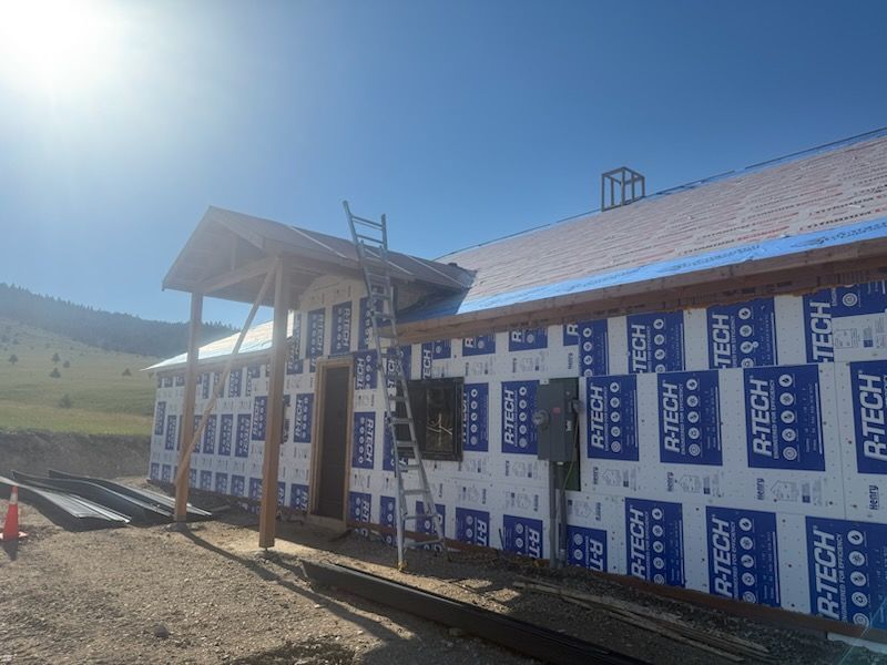 Partially built house with blue and white insulation wrap on a sunny hillside