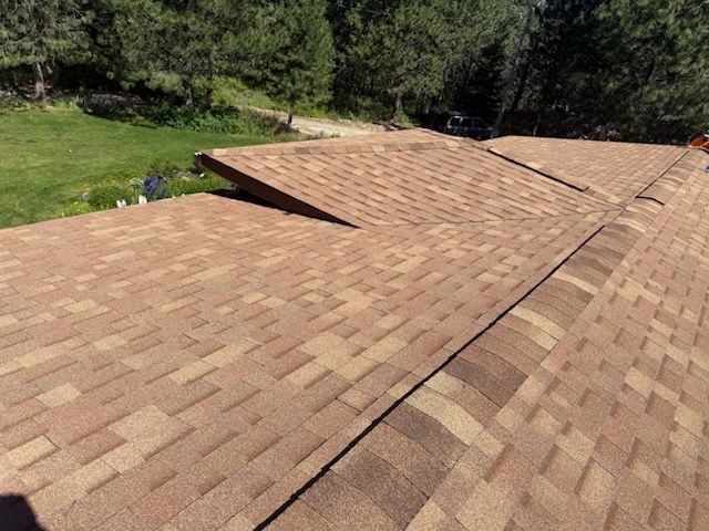 Brown shingle roof with raised sections, set against trees and grass