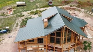 Aerial view of a wooden house under construction with a gray metal roof on a dirt lot.