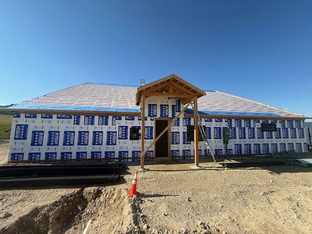 Partially built house with blue housewrap, framed porch, and dirt foreground under a clear sky