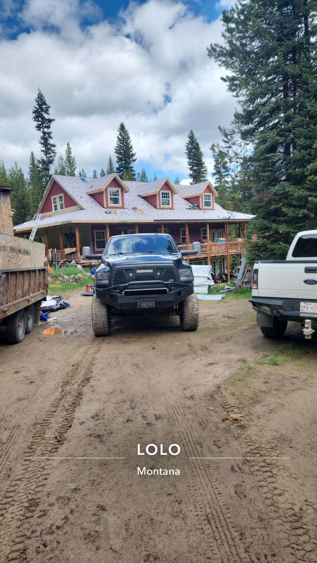 Black truck parked in front of a large house under construction; dirt road.