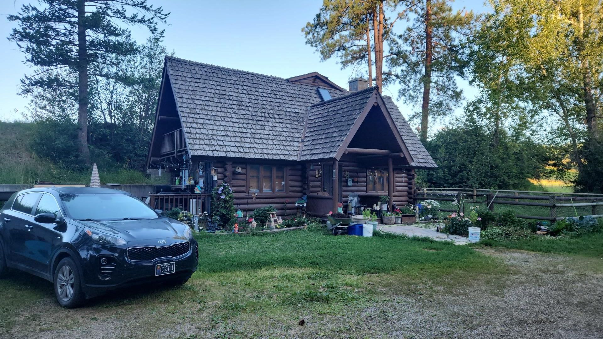 Black car parked near a rustic log cabin with a dark shingled roof, set in a grassy yard.