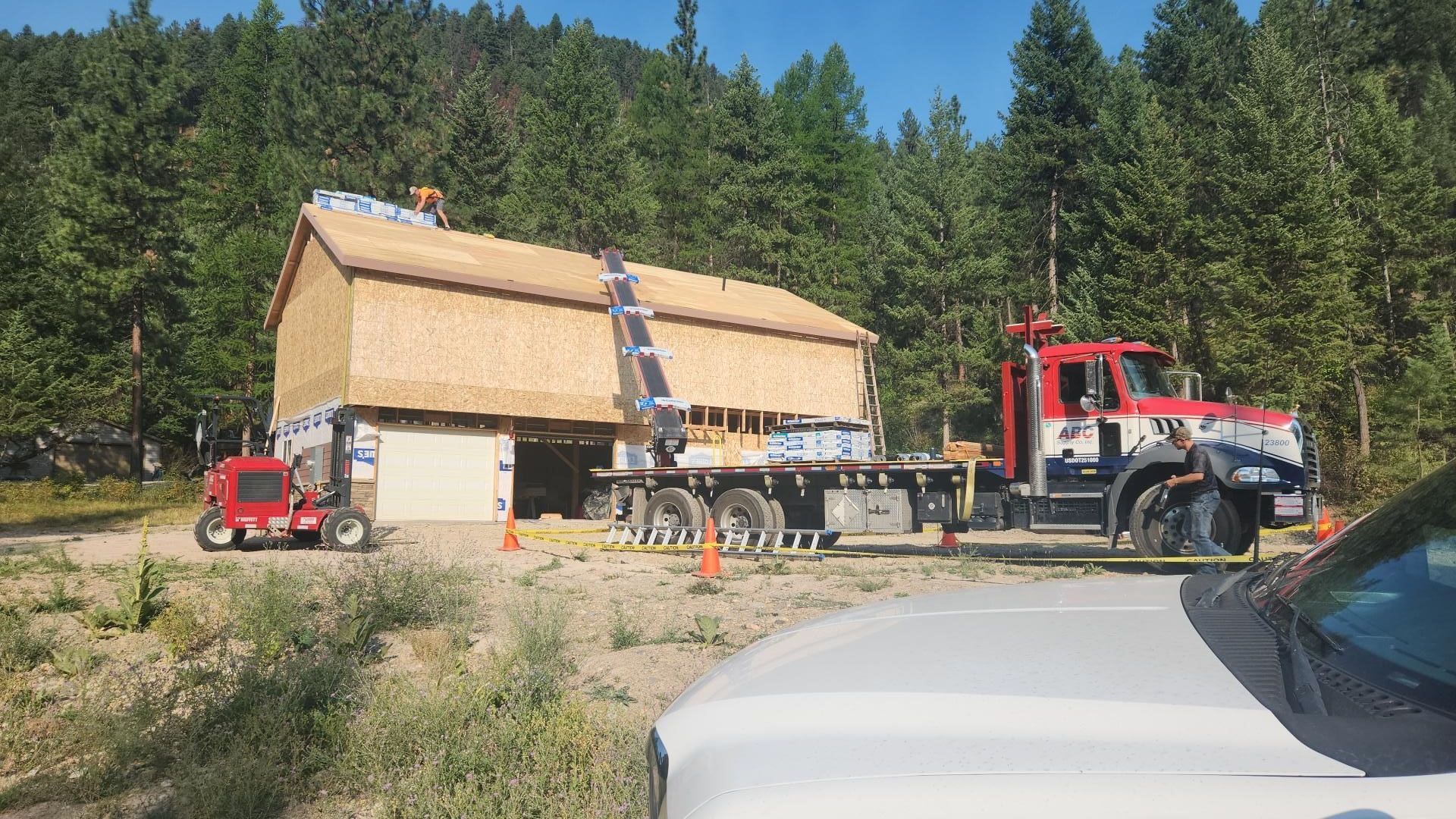 A prefabricated house being lifted onto a foundation by a crane. Construction workers are visible on top of the house.