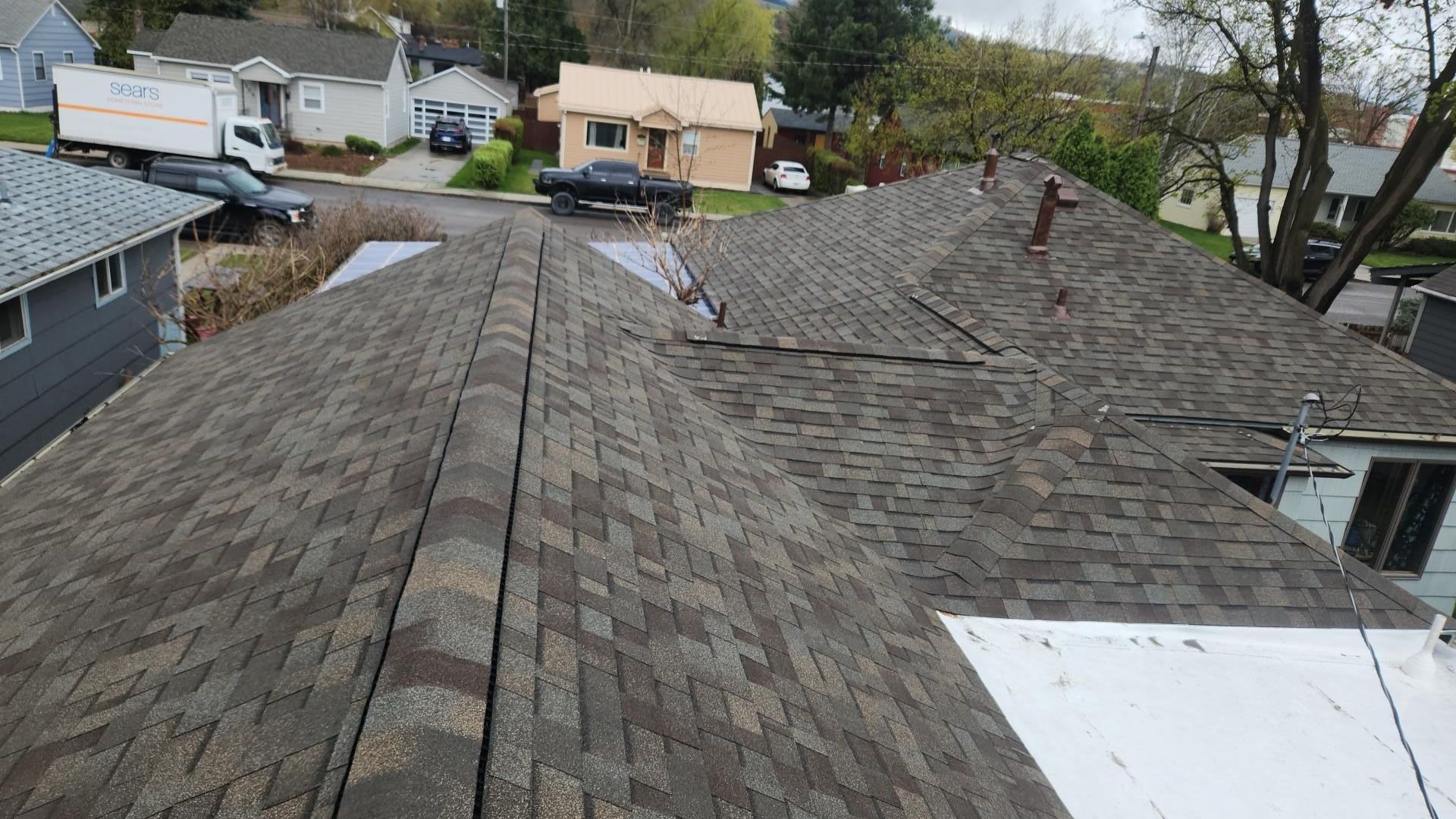 Overhead view of a shingled roof with a crack. Houses and a street visible in the background.
