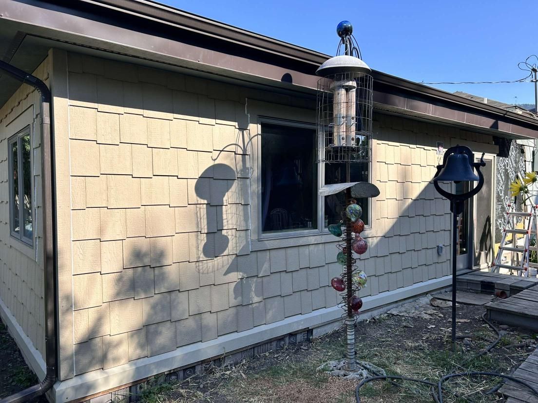 Beige shingled house exterior with brown trim, window, and bird feeder.