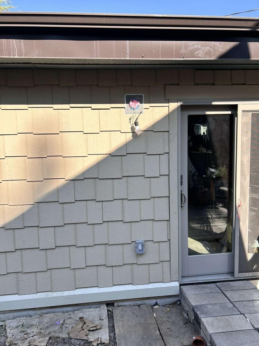 Exterior wall with tan shake siding, sliding glass door, and an electrical outlet.