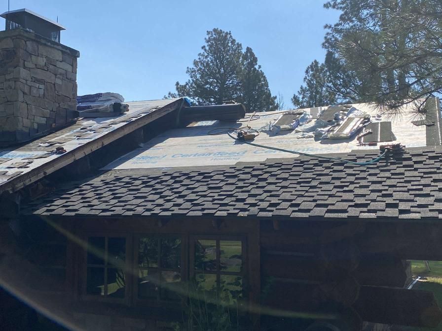 Roof partially under construction on a log cabin with a stone chimney; blue sky in background.