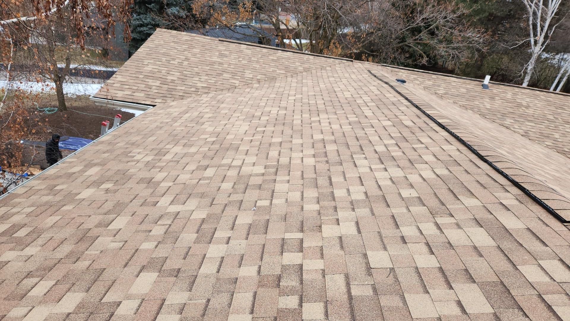 Brown asphalt shingle roof on a house, angled view, sunny day.