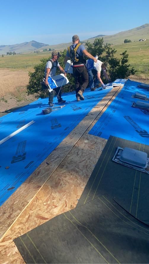 Roofers installing roofing on a sunny day; blue tarp, mountains in the background.