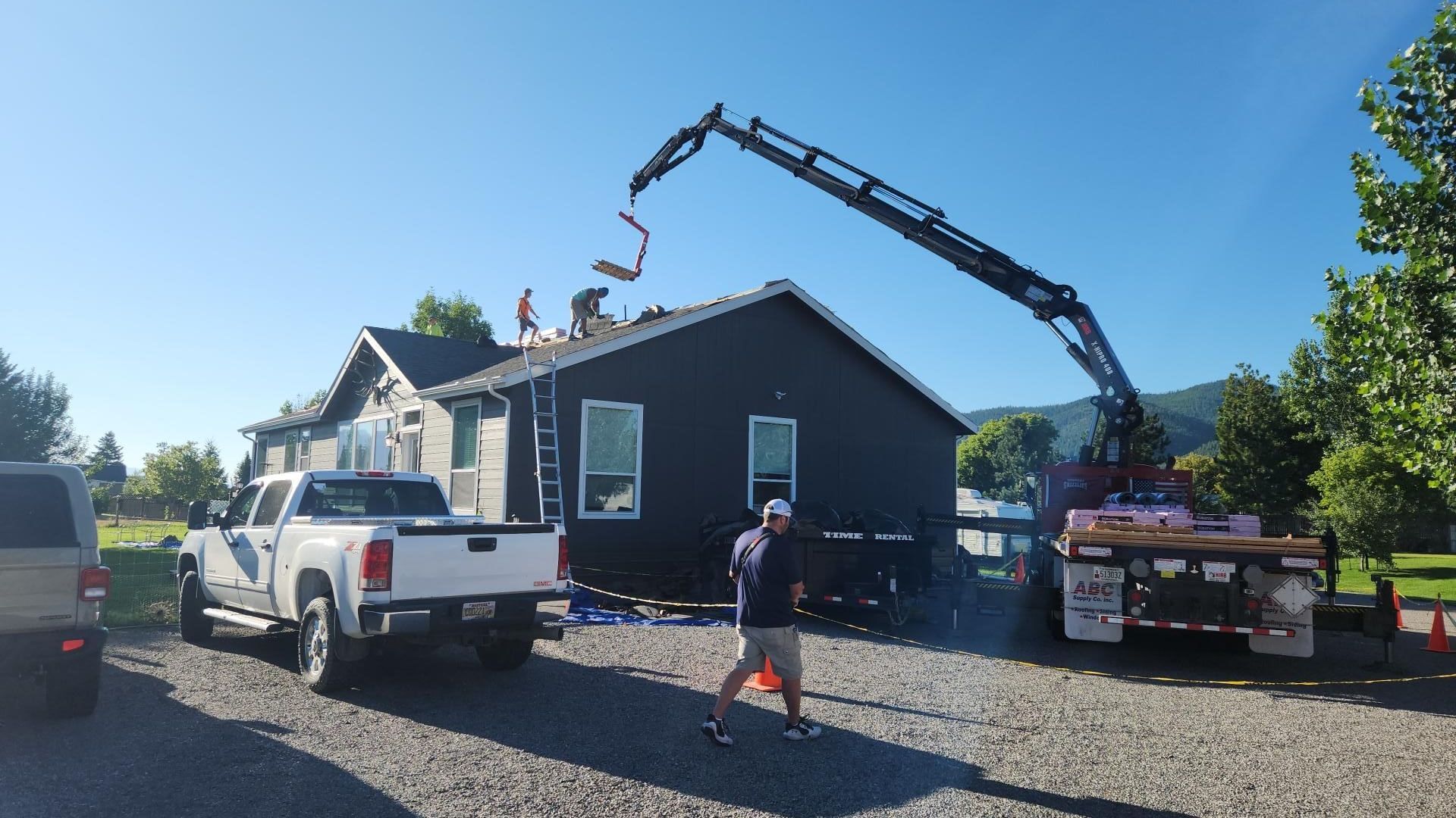 House exterior under construction, concrete being poured onto roof from a truck-mounted boom. Sunny day.