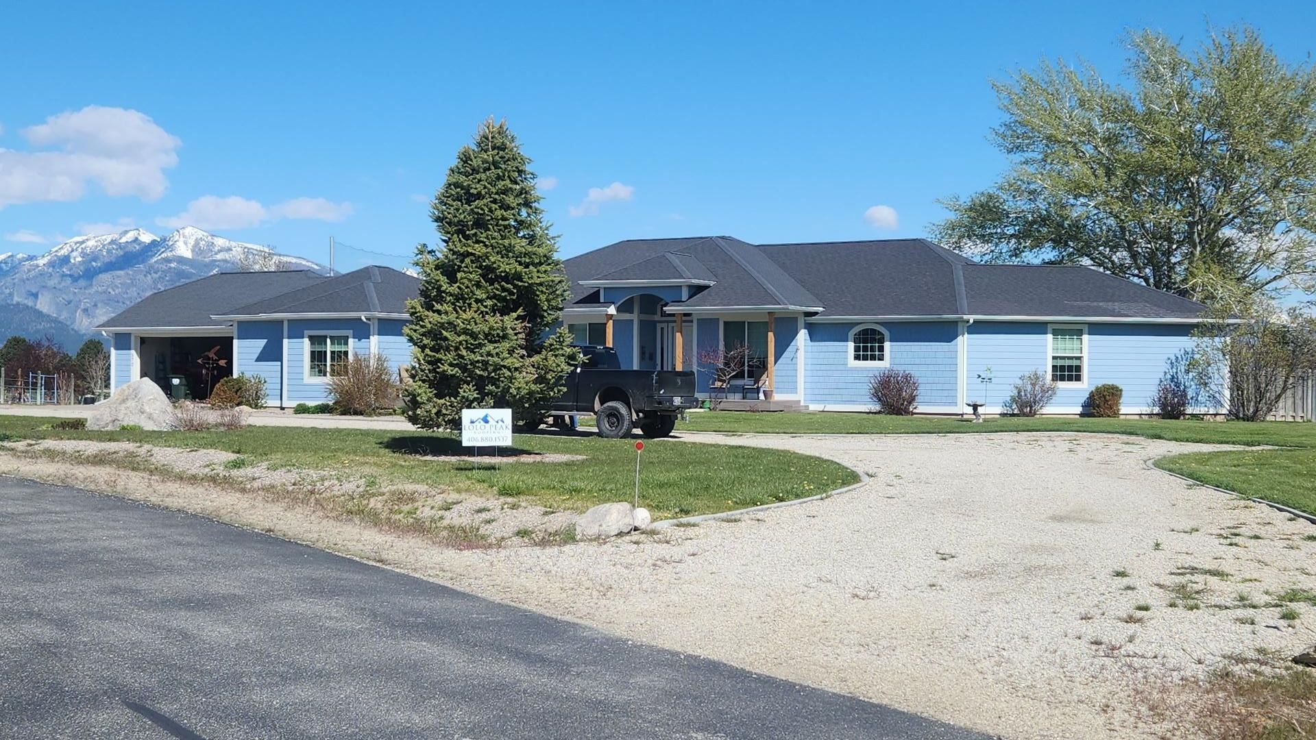 Blue house with gravel driveway and mountain backdrop.