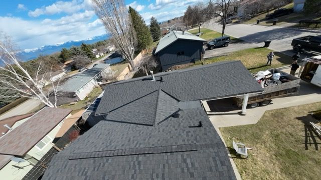 Roofing workers inspecting dark gray shingle roofs in a suburban neighborhood on a sunny day
