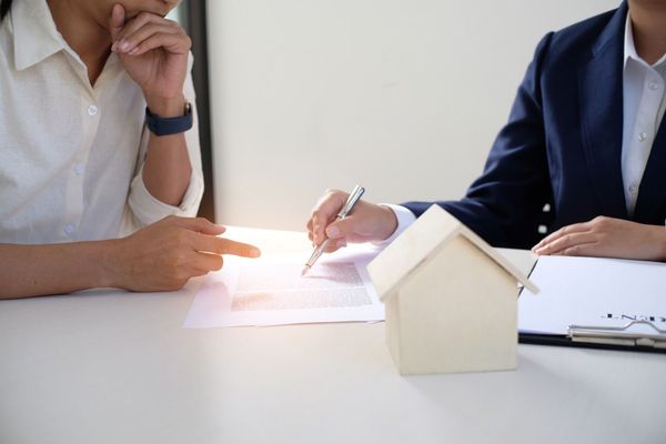 Two people review and sign paperwork beside a small house model