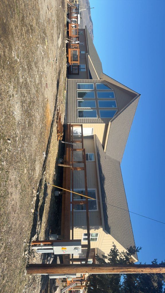 Modern house with a steep roof under construction, with scaffolding and gravel foreground against a blue sky.