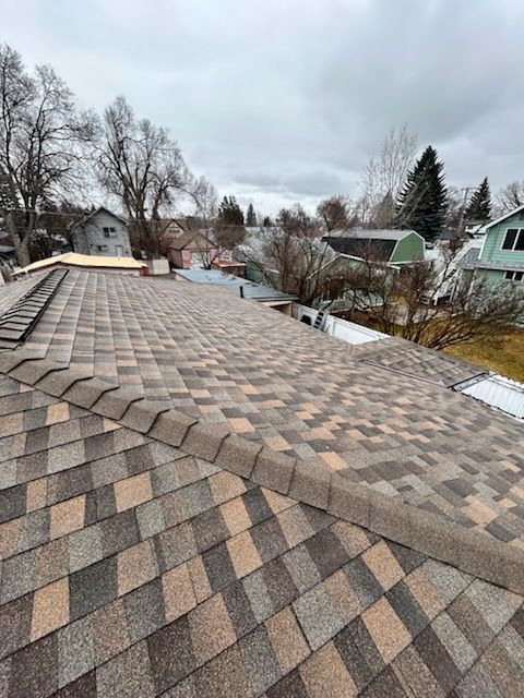Weathered shingle roof with a valley, viewed over a snowy residential neighborhood on an overcast day