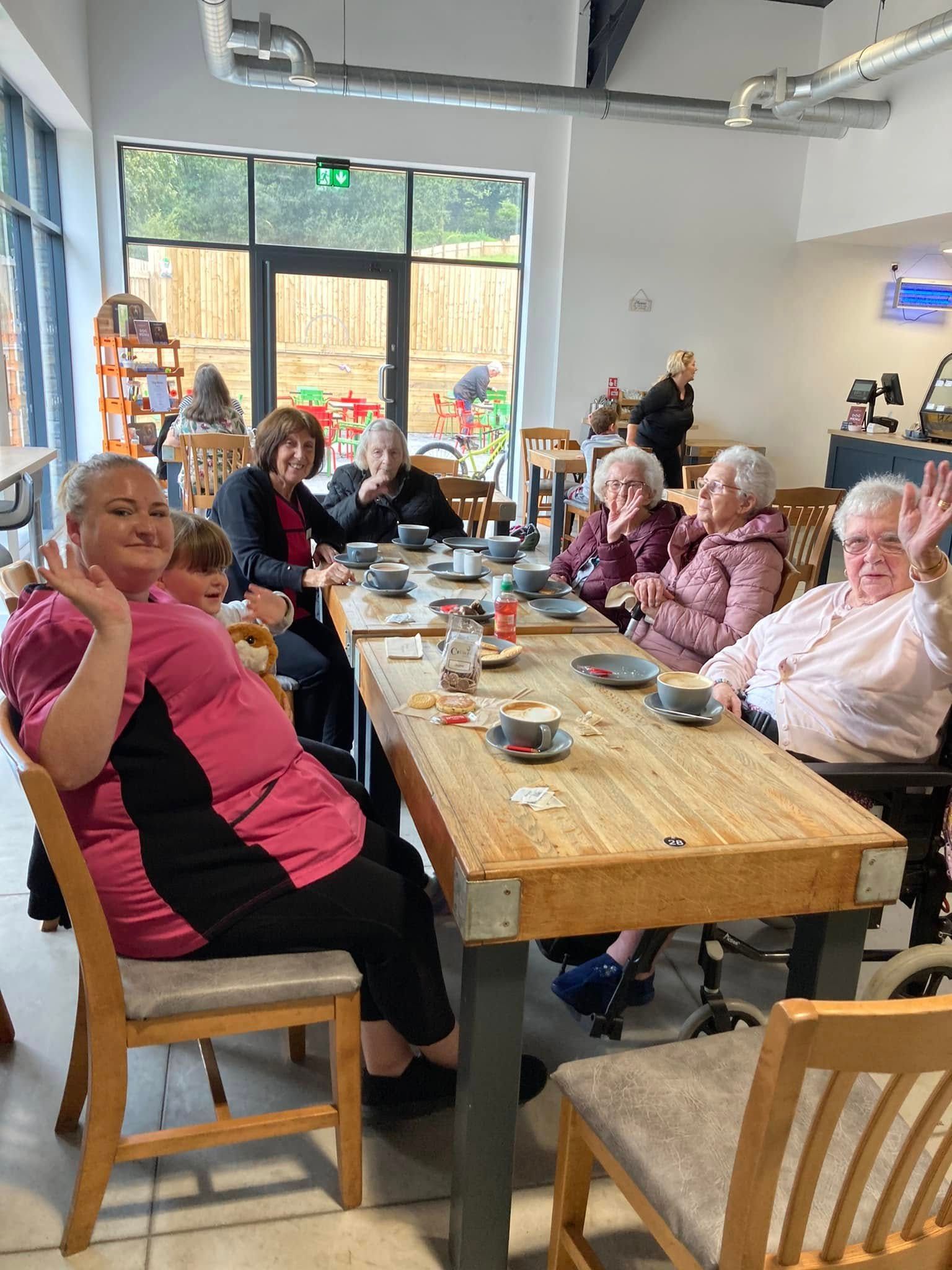People seated around a long table in a bright café, chatting and eating together