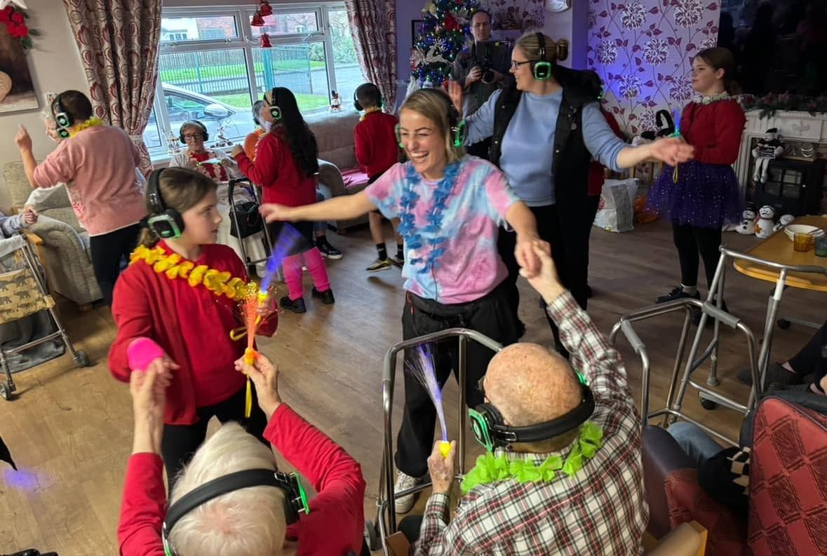 People dancing in a lively indoor gathering with colorful decorations and walkers nearby