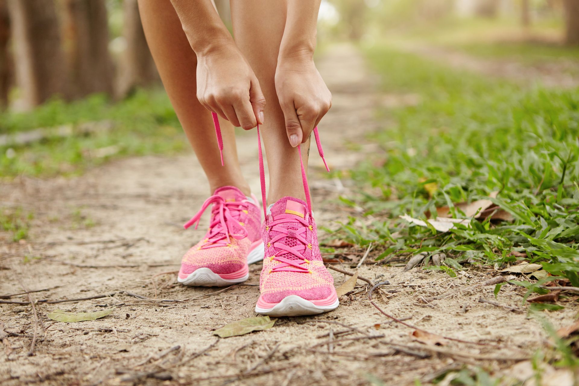 Persona atándose los cordones rosas de los zapatos en un camino de tierra, preparándose para correr.