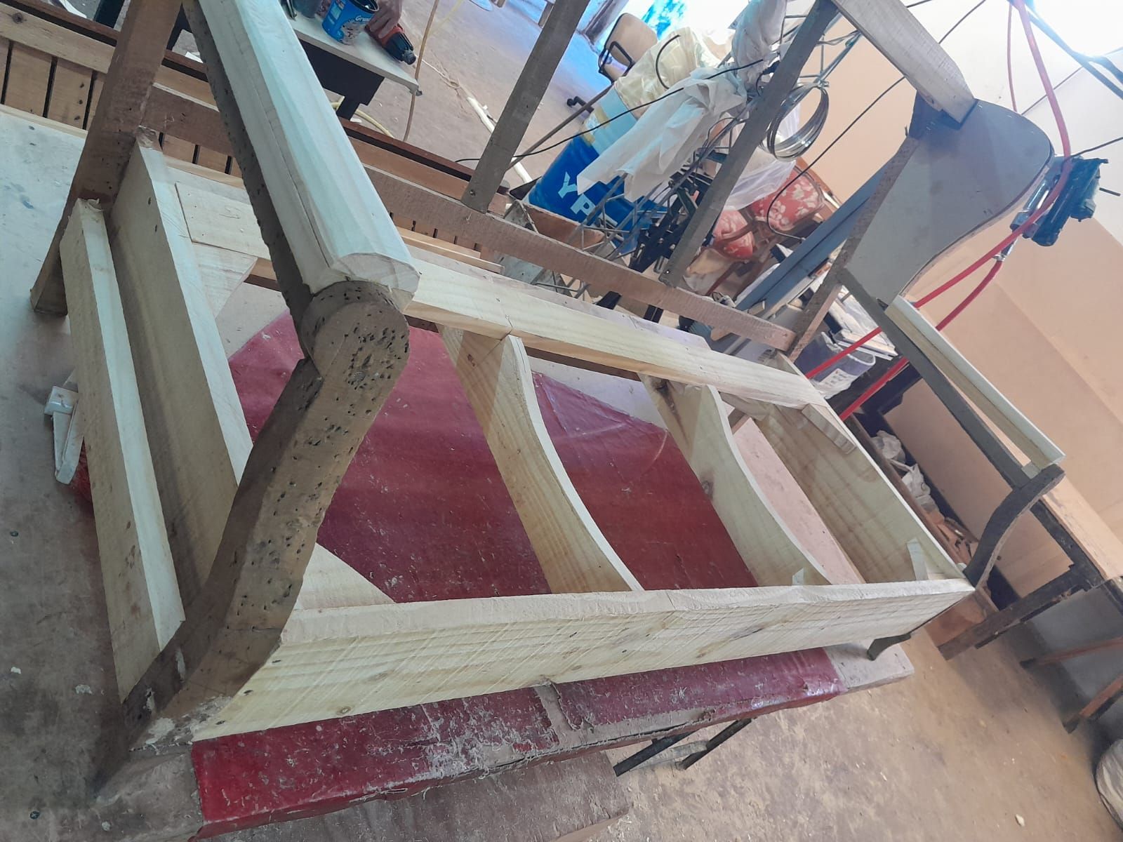 Estructura de cama de madera en proceso de construcción en un taller, con herramientas y materiales cerca.