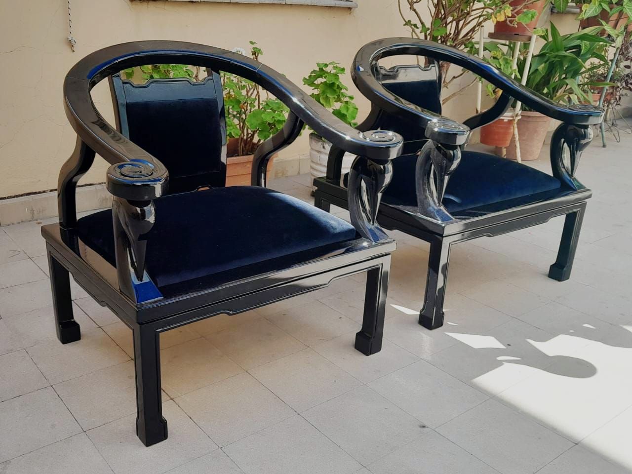 Dos sillones de madera negra con cojines azules en un patio soleado.