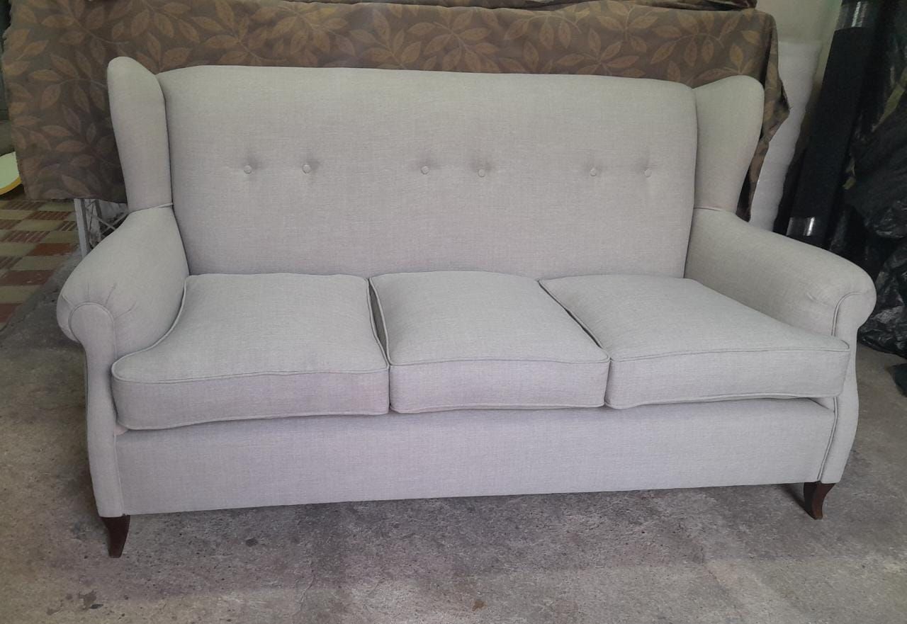 Sofá de dos plazas tapizado en blanco con respaldo capitoné y tres cojines de asiento sobre una alfombra gris.