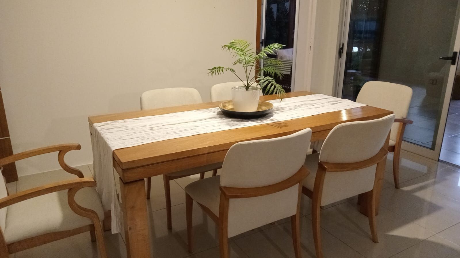 Mesa de comedor moderna con sillas blancas y un jarrón de flores en una habitación luminosa.