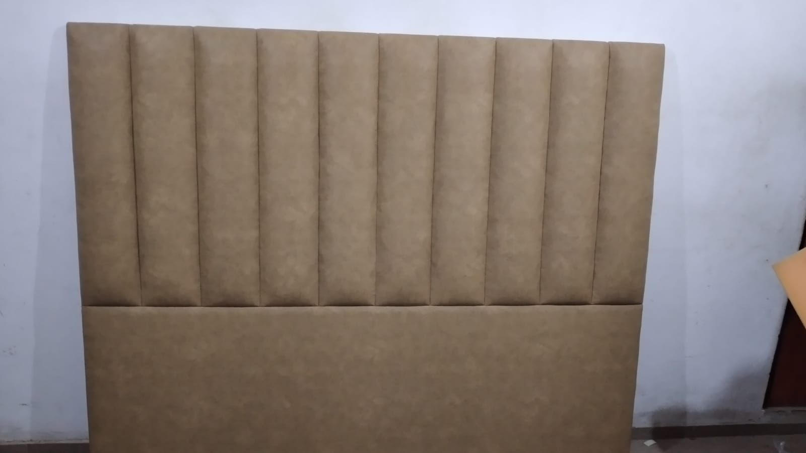 Cabecero tapizado en color beige con capitoné contra una pared lisa, con una mesa de madera en el extremo derecho.