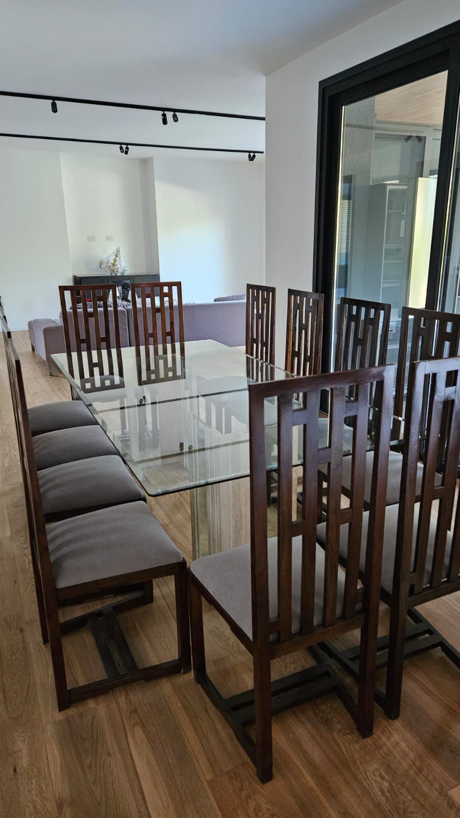Comedor con sillas de madera, una mesa de cristal y un banco sobre un suelo de madera noble.