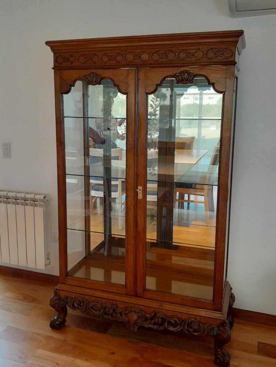 Vitrina de madera ornamentada con cristales y laterales espejados en una habitación luminosa.
