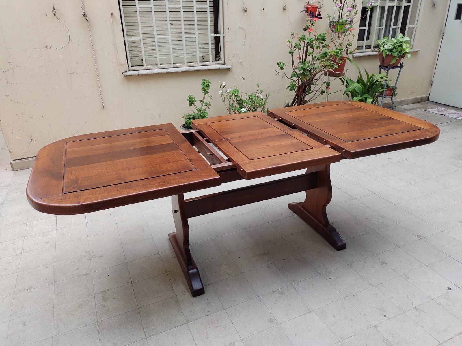Mesa de comedor plegable de madera con dos extensiones, en un patio, acabado marrón.