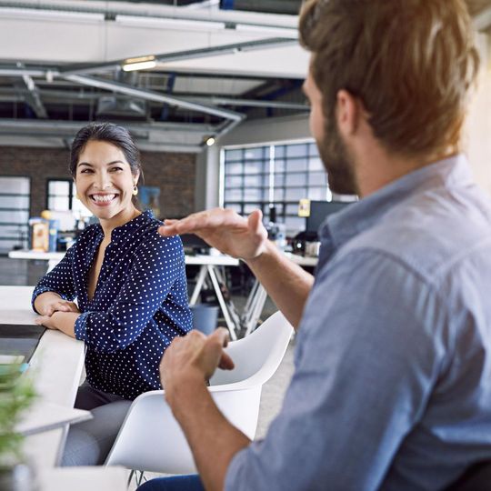 Two people talking in a bright office, one gesturing while the other smiles