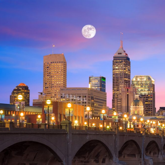 City skyline at dusk with a full moon above illuminated buildings and a bridge in the foreground