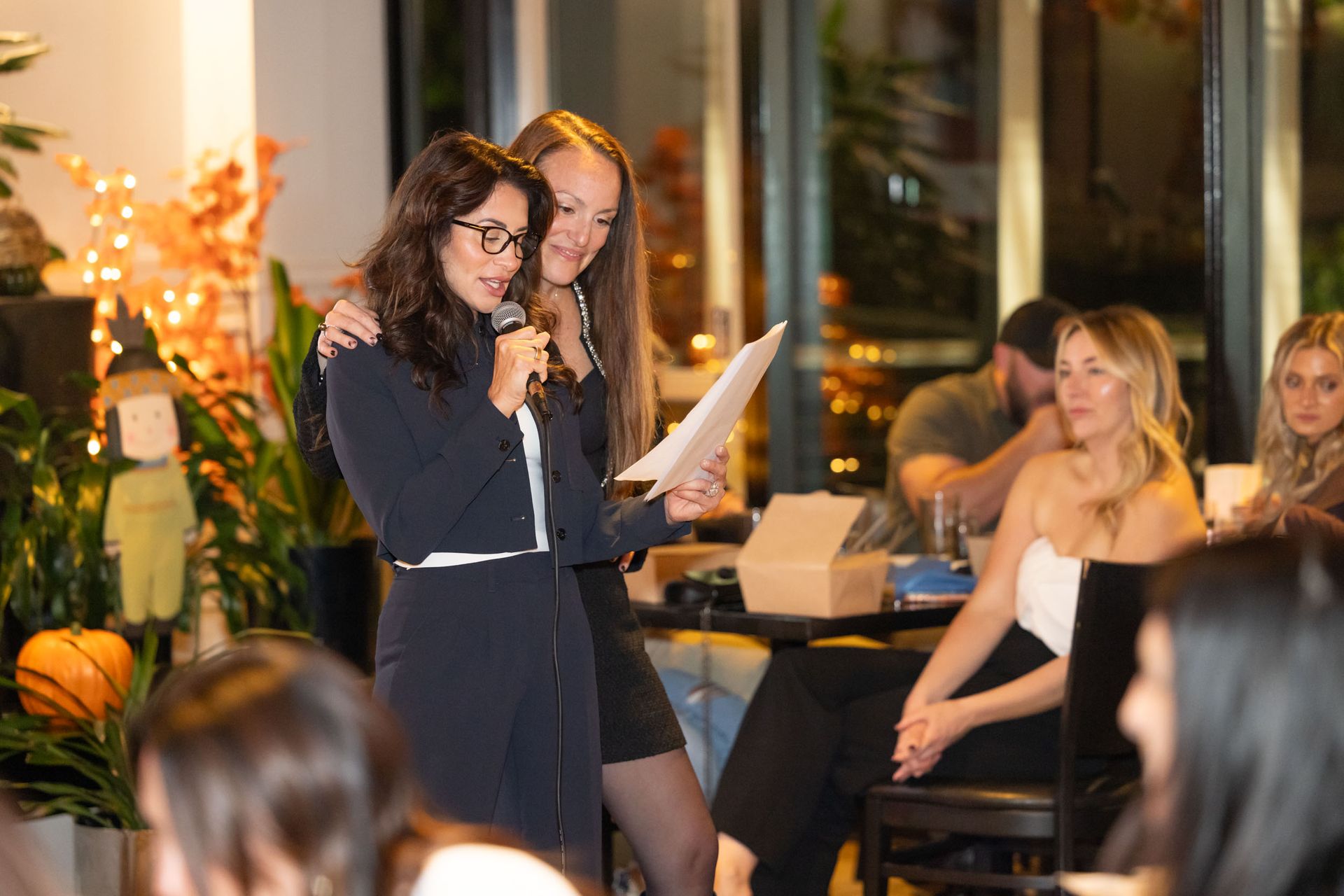 Two women are standing next to each other holding a microphone.