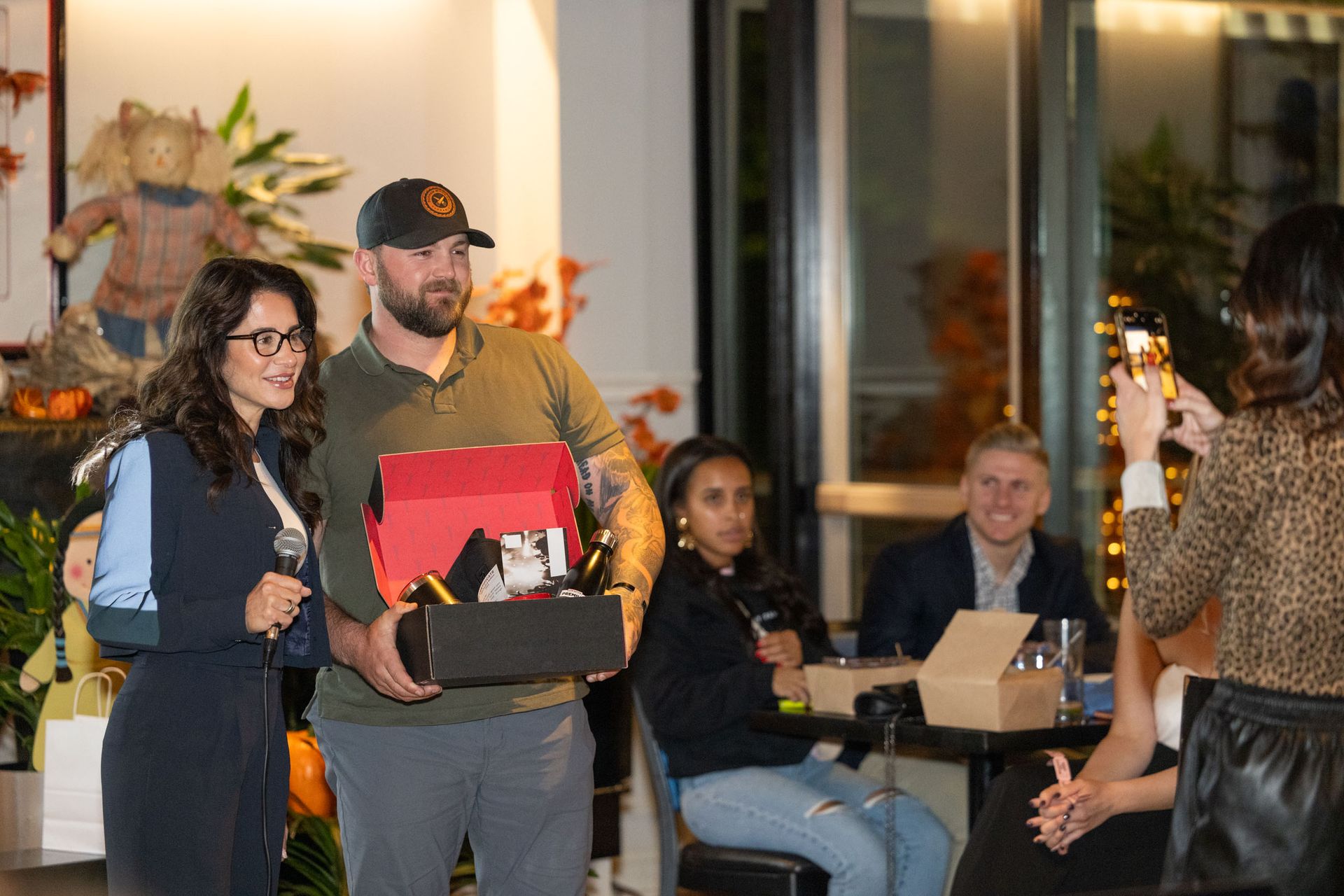 A woman is taking a picture of a man holding a box.