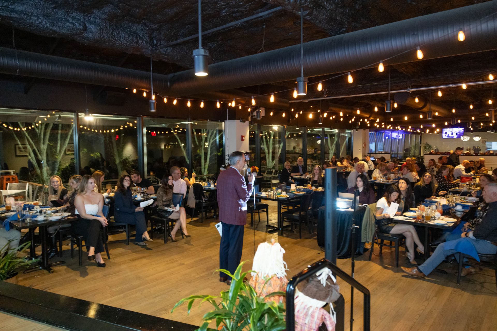 A man is giving a speech in front of a crowd of people in a restaurant.