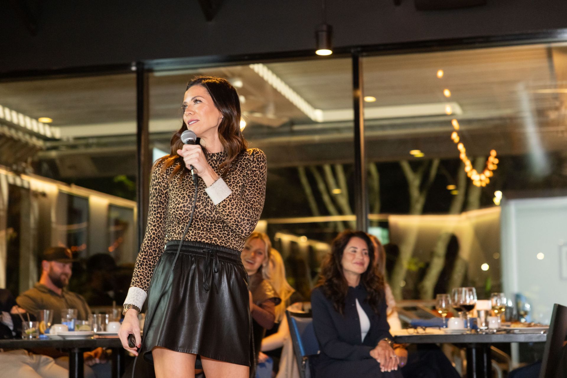 A woman is standing in front of a microphone in a restaurant.