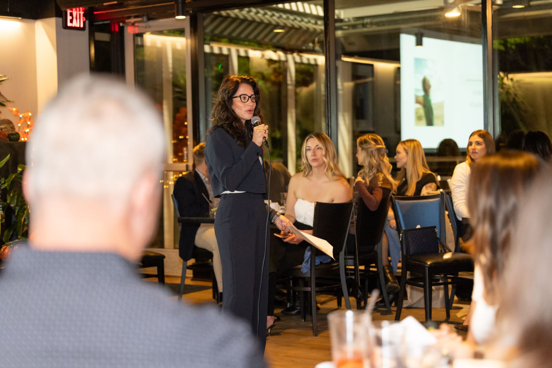 A woman is standing in front of a microphone talking to a group of people.