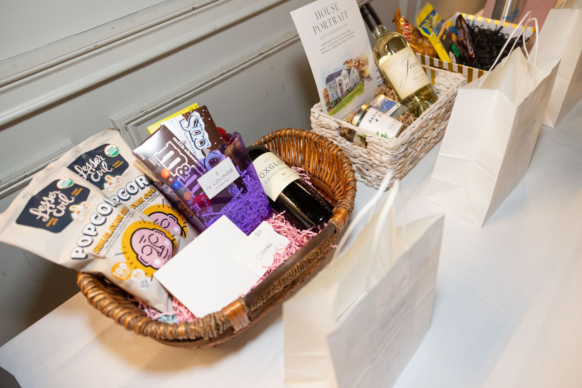 A basket filled with snacks and wine bottles on a table.