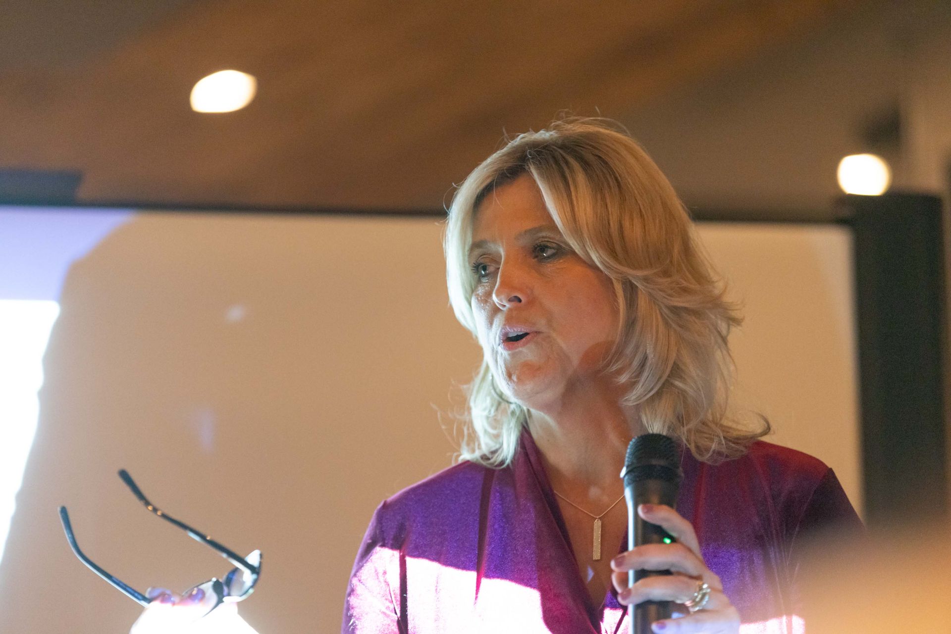 A woman is holding a microphone and wearing glasses.