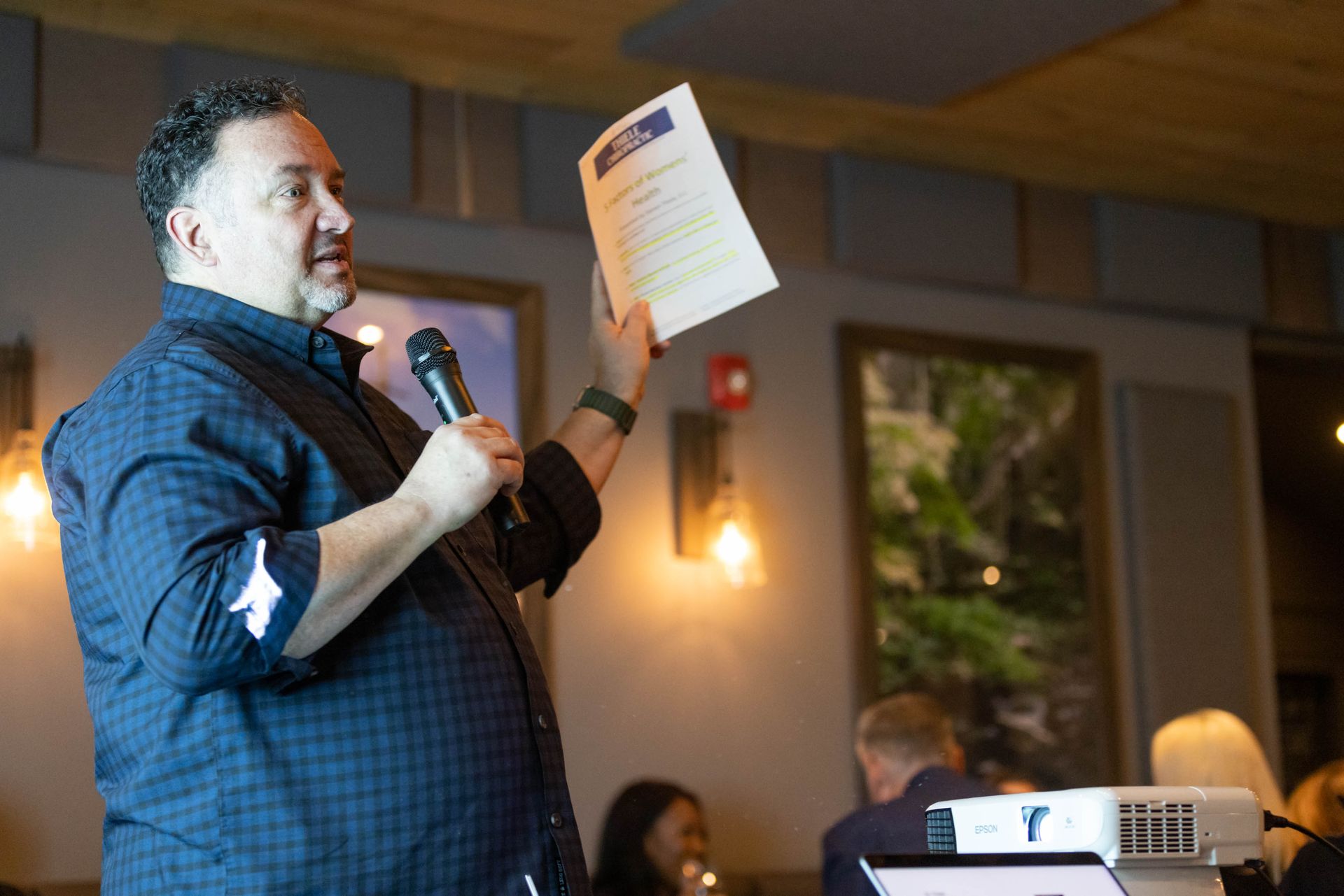 A man is holding a piece of paper and speaking into a microphone.