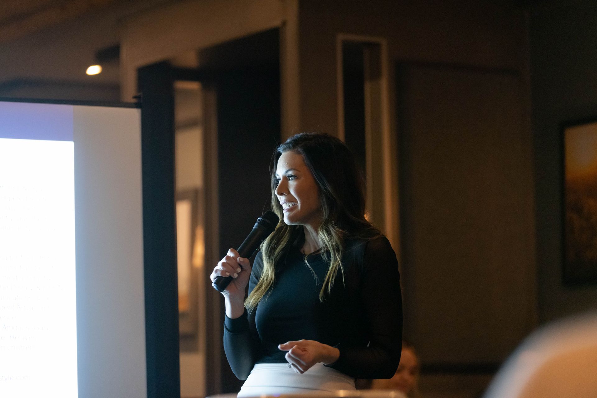 A woman is holding a microphone in front of a projector screen.