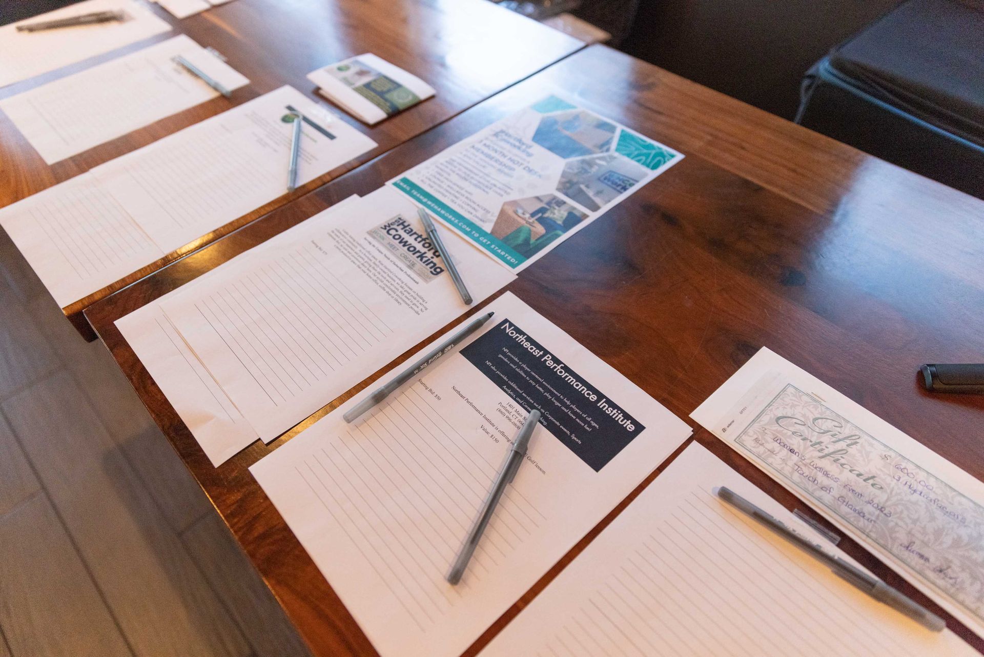 A wooden table with papers and pens on it