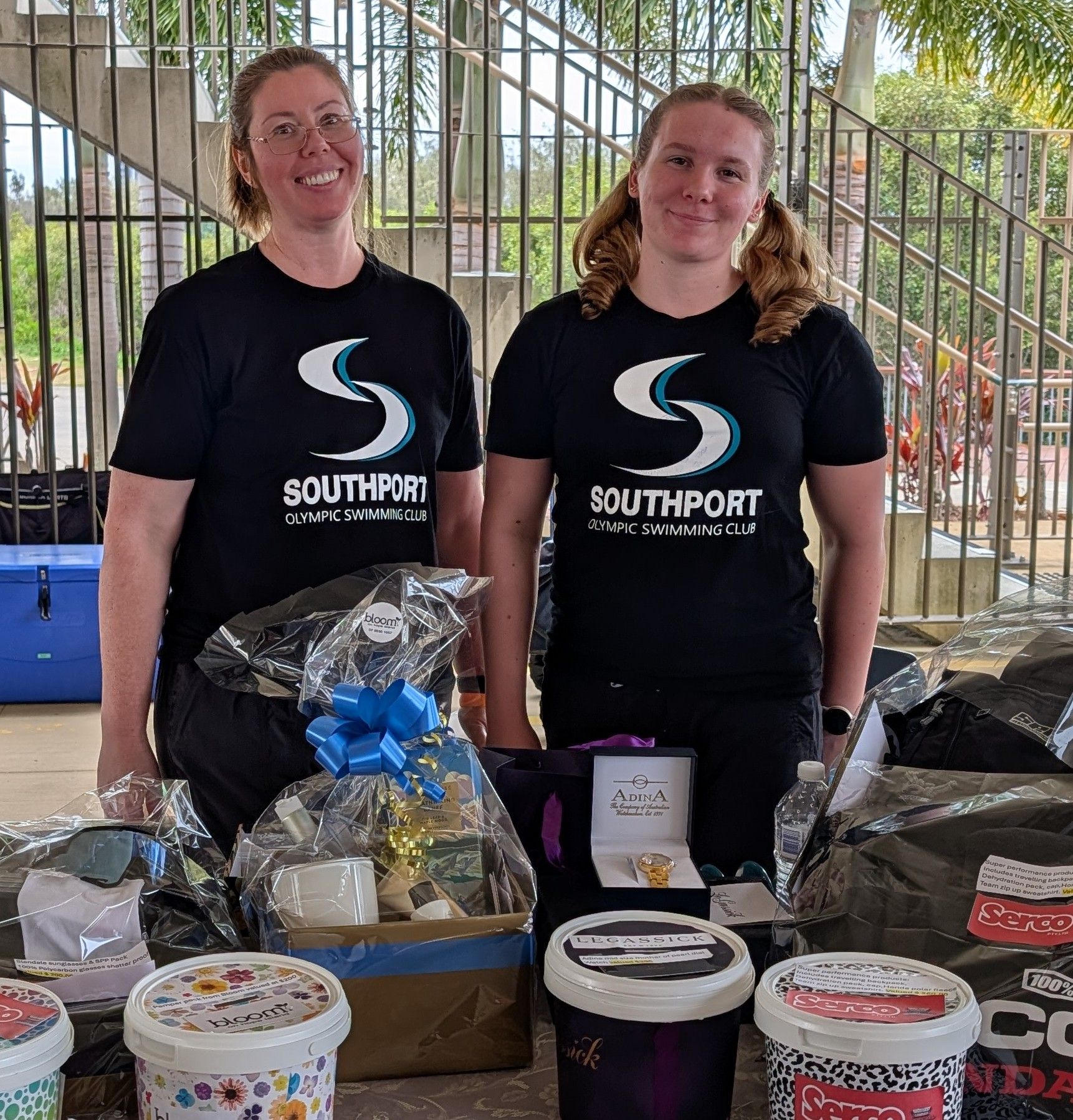 Two women at a table with Southport merchandise, smiling. Outdoor setting.